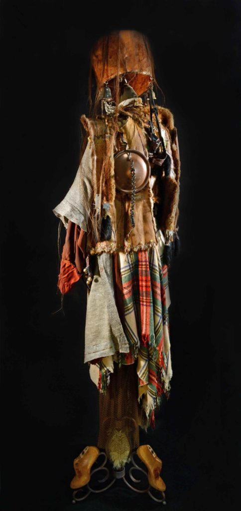 Shamanic Vestments For A Feminine Field Marshall Assemblage 2016 84 x 36 x 34 inches by Leslie Ann McQuaide, Antique lampshade, horse tail, artist's blood, feather duster, steel chain mail necklace, antique sieve, silver and brass bells, vintage welding goggles, copper chafing dish lid, vintage telephone receiver, vintage muskrat coat with linings and inter-facings, ammo bullet belt, sequined belly-dancing brassiere, WWII Pacific Theater decorative medals brass backings, silk Celtic knots, nut-processing conveyor belt gears, Tibetan chimes, rabbits' feet, steel drawer plates, piano felts, vintage Stewart tartan blanket, antique women's shoe forms, lamp base, lamb's wool, fireplace screen, beads, and encaustic